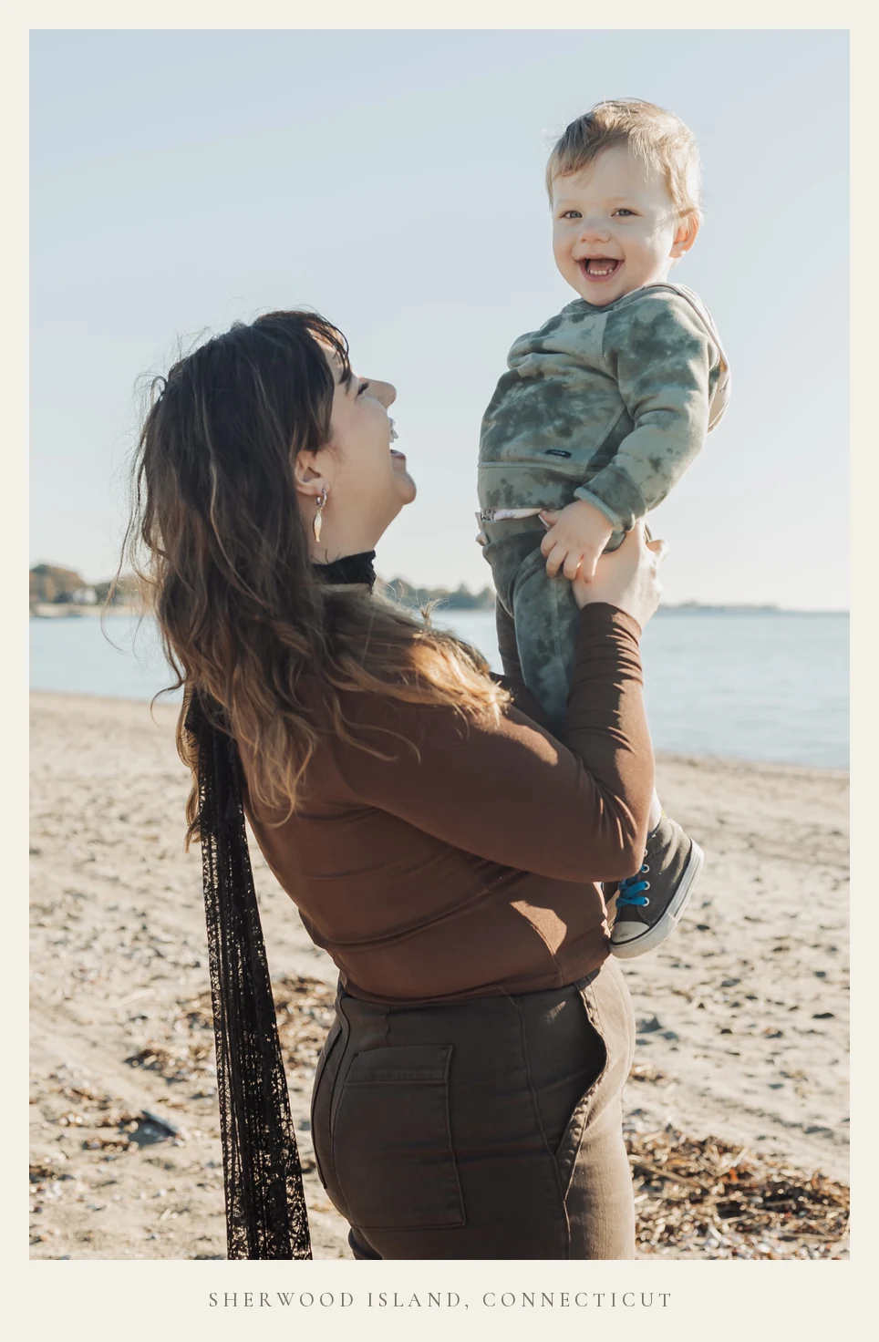 Miranda Sita lifting her son overhead on the beach at Sherwood Island State Park in Westport, Connecticut, both laughing, Long Island Sound behind them. Captioned: Sherwood Island, Connecticut.